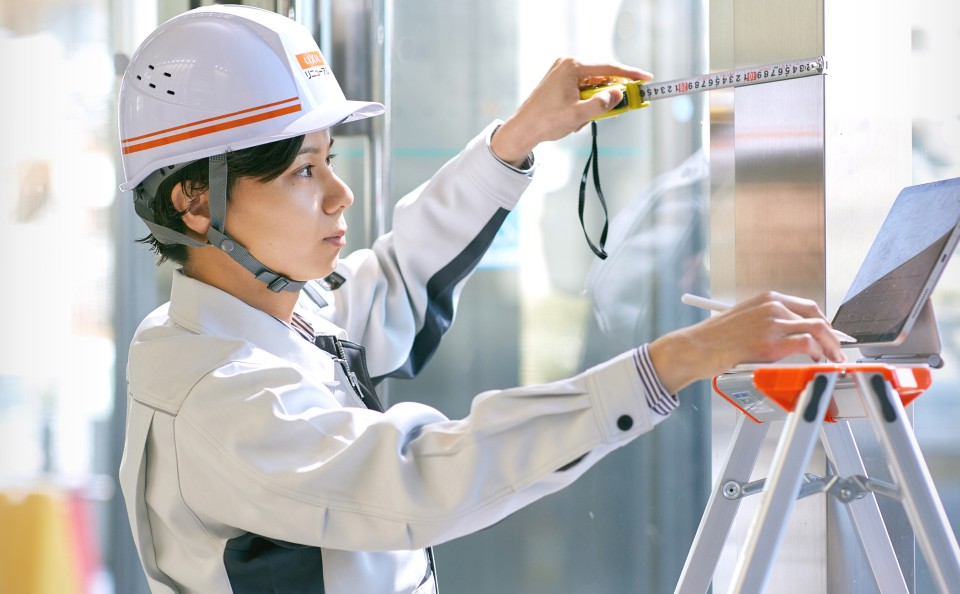 メジャーで長さを測っている作業着を着た施工管理職の女性。